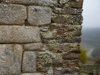 Lozère castle wall detail with weathered granite and schist stones, moss and lichen, under soft autumn morning light, no people visible